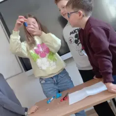 Dzieci przeprowadzają eksperyment z magnesem, trzymając go nad łańcuszkiem.